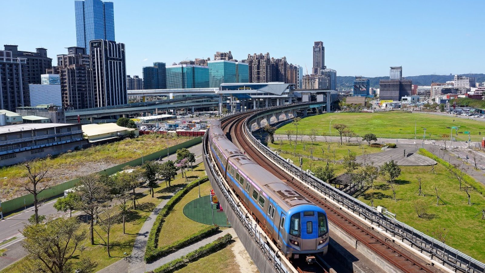 A metro train of Taoyuan Airport MRT travels on the elevated railway track, with high rise buildings booming in the Industrial Park in background, in Xinzhuang District, New  Taipei City, Taiwan, Asia